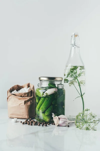 Glass jar with preserved cucumbers, glass bottle with dill and salt on table — Stock Photo