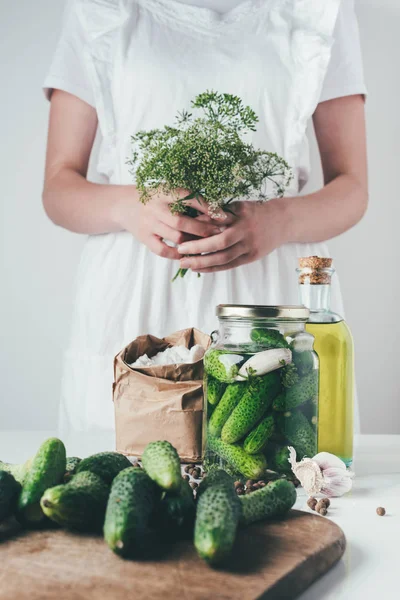 Cropped image of woman preparing preserved cucumbers and holding dill at kitchen — Stock Photo