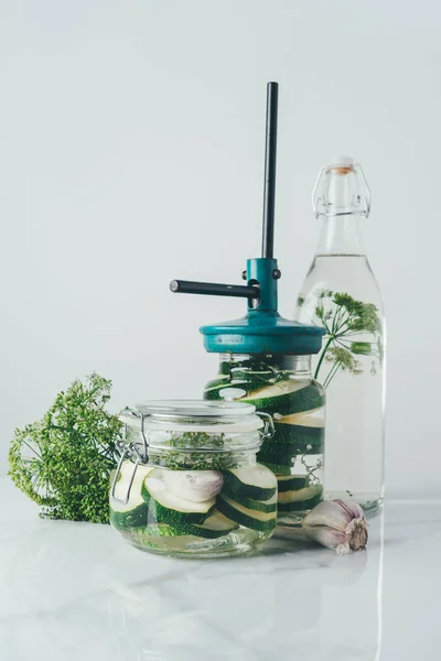 Glass jars and bottle with zucchini and dill for preserving on kitchen table — Stock Photo