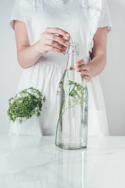 Imagen recortada de la mujer botella de vidrio de cierre con agua y eneldo en la cocina - foto de stock