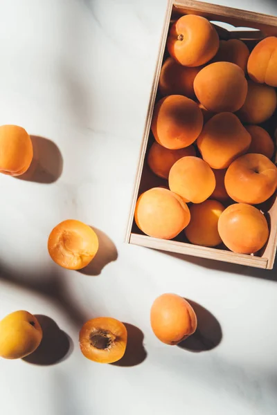 Flat lay with ripe apricots in wooden box on light marble surface — Stock Photo