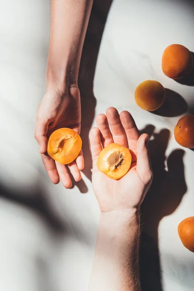 Partial view of man and woman with pieces of ripe apricots in hands on light marble surface — Stock Photo