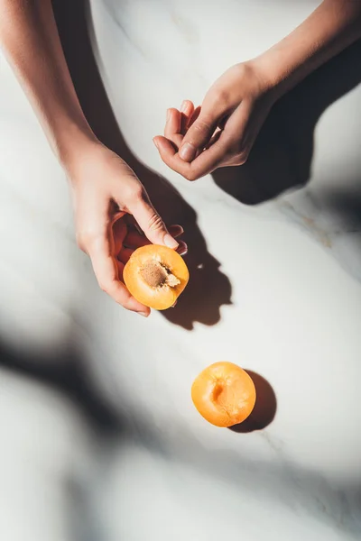Partial view of woman holding piece of apricot on light marble surface — Stock Photo