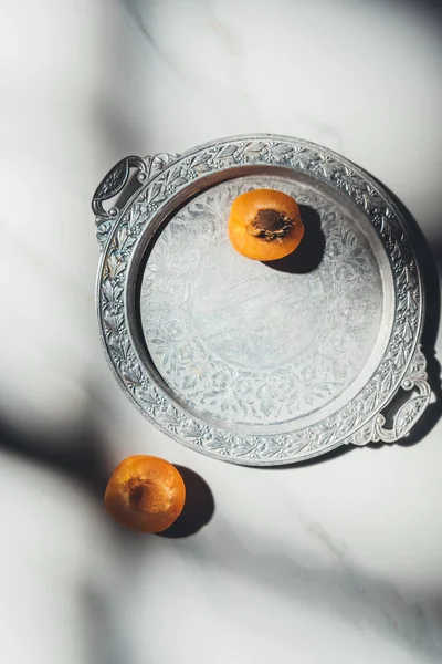 Вид сверху на куски спелого абрикоса на металлическом подносе и светлом мраморном столе — стоковое фото