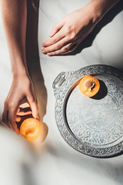 Teilansicht einer Frau, die ein Stück Aprikose auf heller Marmoroberfläche hält — Stockfoto