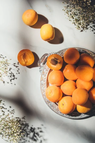 Plat avec des abricots mûrs sur plateau métallique avec des fleurs de gypsophile sur table en marbre clair avec des ombres — Photo de stock