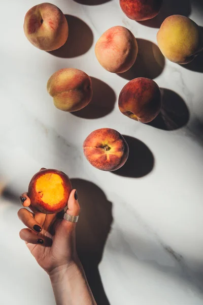 Partial view of female hand and ripe peaches on light marble tabletop with shadows — Stock Photo