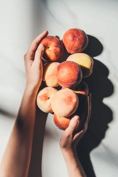Cropped shot of woman holding fresh and ripe peaches on light marble surface — Stock Photo