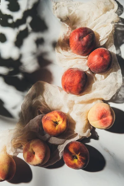 Flat lay with ripe peaches and gauze on light marble tabletop with shadows — Stock Photo