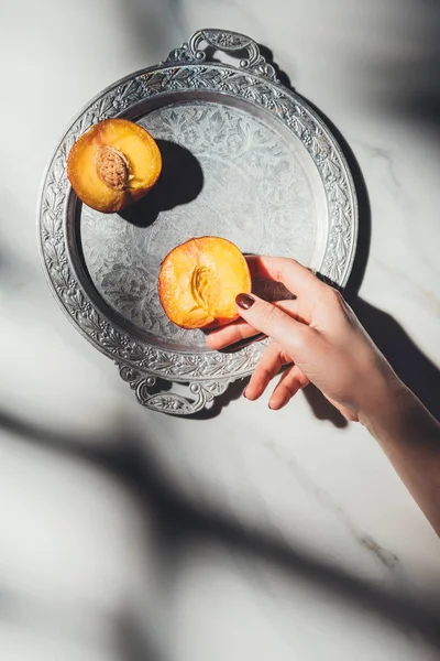 Tiro cortado de mulher segurando peça de pêssego na bandeja de metal na superfície de mármore leve — Fotografia de Stock