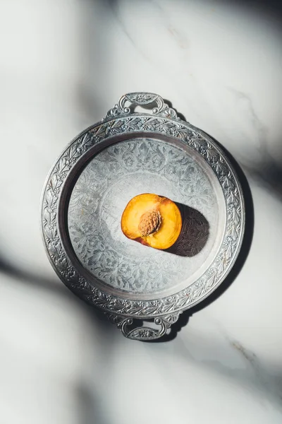 Top view of piece of peach on metal tray on light marble tabletop with shadows — Stock Photo