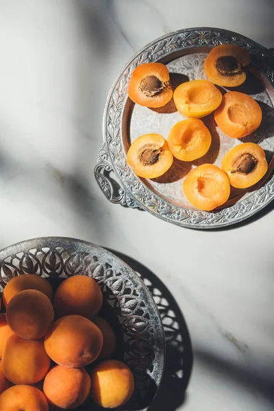 Flat lay with fresh apricots in metal bowl and on tray on light marble surface with shadows — Stock Photo