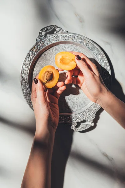 Partial view of woman holding pieces of fresh apricot on metal tray on light marble surface — Stock Photo