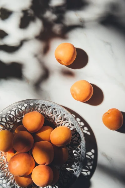 Flat lay with ripe apricots in metal bowl on light marble surface with shadows — Stock Photo