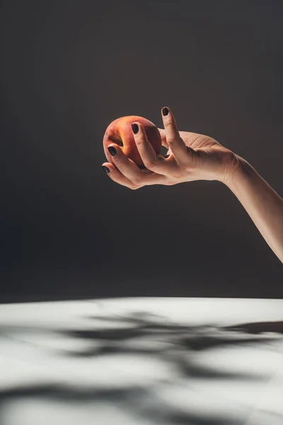 Частковий вид жінки, що тримає стиглий персик в руці на чорному тлі — стокове фото