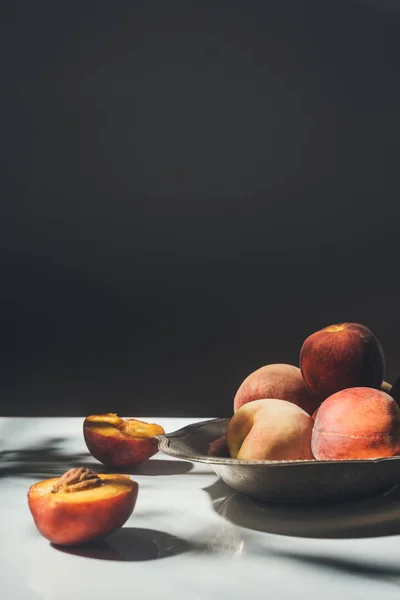 Food composition with ripe peaches in metal bowl on black backdrop — Stock Photo