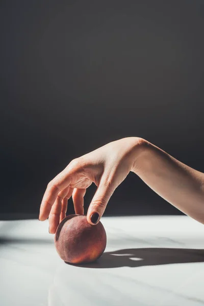 Partial view of woman holding ripe peach in hand on black background — Stock Photo