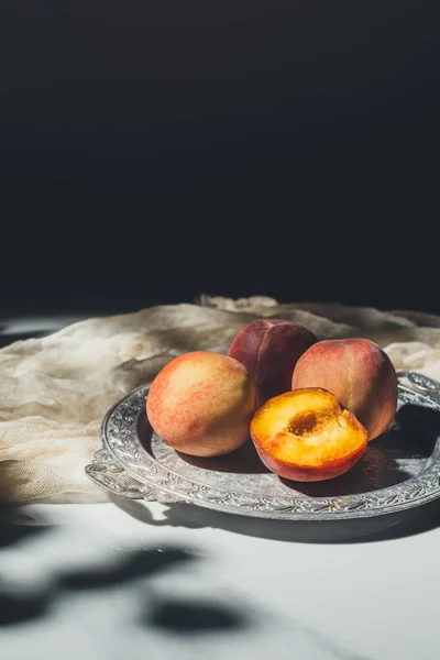 Food composition with ripe peaches on metal tray on marble tabletop with black background — Stock Photo