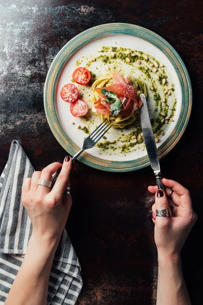 Teilansicht einer Frau, die Pasta mit Minzblättern, Marmelade, Pinienkernen, Pesto und Kirschtomaten isst, die am Tisch mit geriebenem Parmesan bedeckt sind — Stockfoto