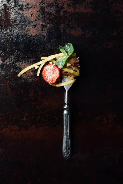 Top view of fork wrapped by pasta with mint leaves, jamon and cherry tomatoes covered by grated parmesan on table — Stock Photo