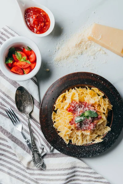 Vue du dessus de l'assiette avec pâtes, parmesan râpé, bols avec sauce et tomates cerises sur table en marbre — Photo de stock