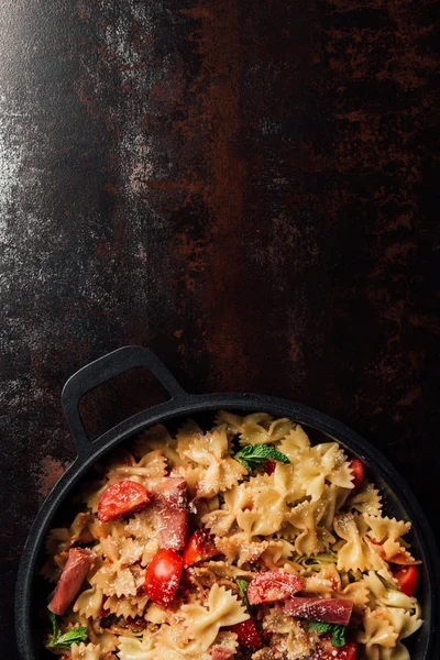 Top view of pasta with jamon, cherry tomatoes, mint leaves covered by grated parmesan in pan on table — Stock Photo