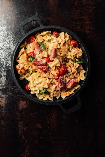 Top view of pasta with jamon, cherry tomatoes, mint leaves covered by grated parmesan in pan on table — Stock Photo