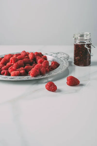 Selective focus of silver tray with raspberries and jar of jam on marble table — Stock Photo