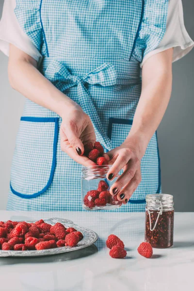 Imagen recortada de la mujer en delantal haciendo mermelada de frambuesas sobre la mesa — Stock Photo