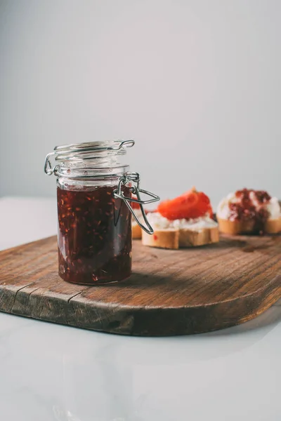 Selective focus of jar with fruit jam on cutting board on grey — Stock Photo