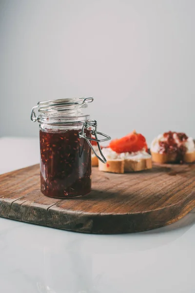 Selektiver Fokus des Glases mit Fruchtmarmelade auf Schneidebrett auf grau — Stockfoto