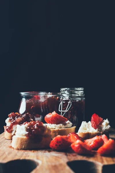 Selective focus of sandwiches with cream cheese, strawberry slices and fruit jam on cutting board on black — Stock Photo