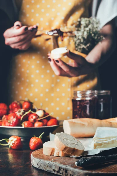 Cropped image of woman in apron spreading strawberry jam on baguette — Stock Photo