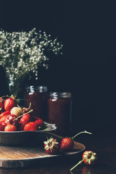 Foyer sélectif de fraises dans un plateau d'argent, fleurs et confiture dans des pots sur noir — Photo de stock