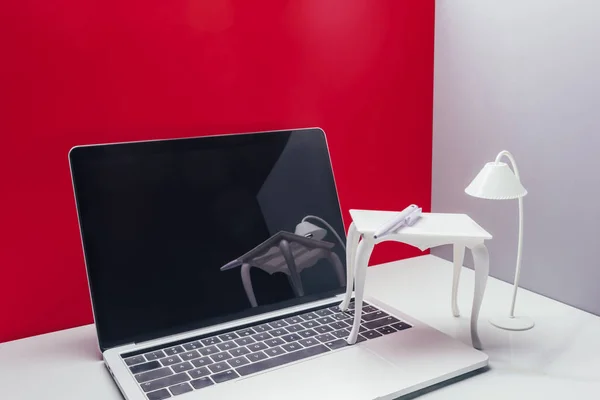 Portátil de tamaño real con mesa de juguete y lámpara en miniatura habitación roja - foto de stock