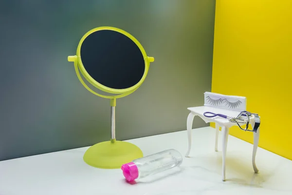 Зеркало для макияжа и туалетный столик с бутылкой лосьона и бигуди для ресниц в миниатюрной комнате — стоковое фото