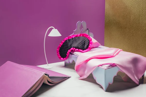 Cama de juguete y lámpara de antorcha con máscara de dormir de tamaño real y libro en habitación en miniatura - foto de stock