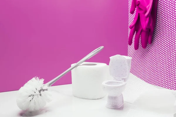 Toy toilet with real size toilet brush and paper towel roll in miniature room with rubber gloves hanging on wall — Stock Photo