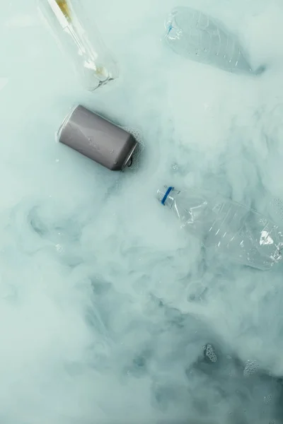 Vista superior da fumaça, lata e garrafas plásticas que fluem na água, conceito da proteção ambiental — Fotografia de Stock