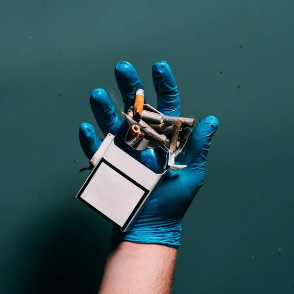 Partial view of man in latex glove holding cigarettes in hand, ecosystem protection concept — Stock Photo
