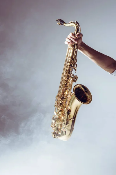 Mano sobre joven músico sosteniendo saxofón en humo sobre gris - foto de stock