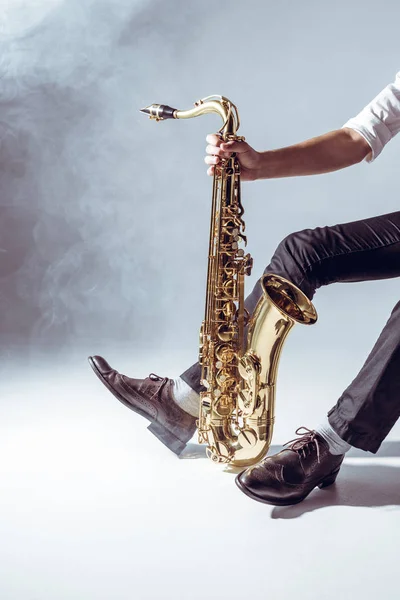 Recortado disparo de profesional joven músico sosteniendo saxofón en gris - foto de stock