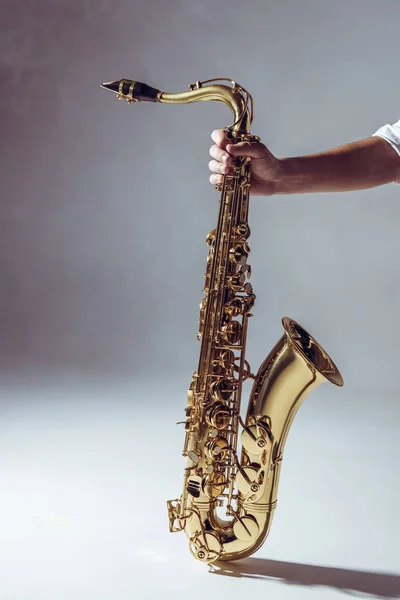 Gros plan vue partielle de l'homme tenant un saxophone en fumée sur fond gris — Photo de stock