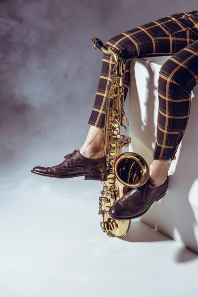 Sección baja de músico profesional sentado con saxofón en humo sobre gris — Stock Photo