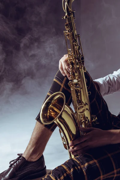 Cropped shot of stylish musician holding saxophone in smoke on grey — Stock Photo