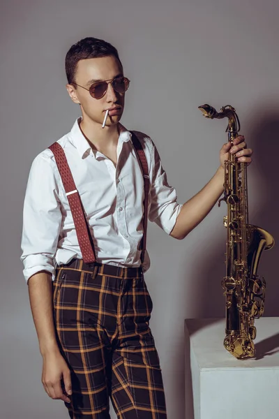Elegante giovane musicista con sassofono portasigarette su grigio — Foto stock