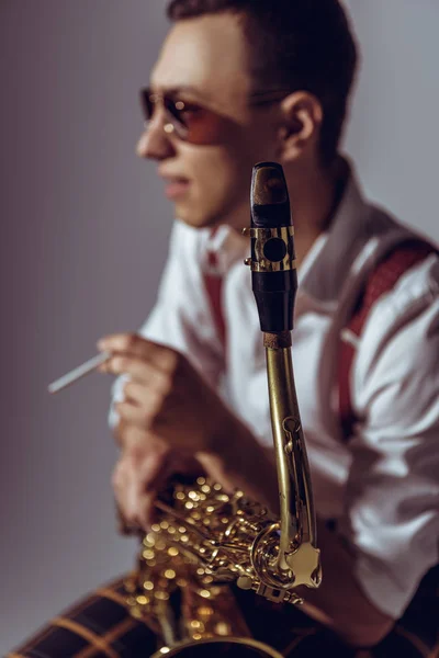 Enfoque selectivo del joven saxofonista fumando cigarrillo en gris - foto de stock
