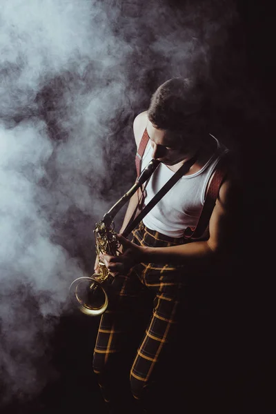 Visão de alto ângulo de jovem músico elegante tocando saxofone em fumaça no preto — Fotografia de Stock