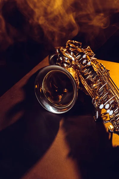 Vista de cerca del saxofón brillante en humo y retroiluminado en negro - foto de stock