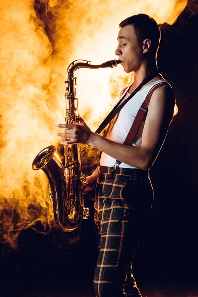 Vista lateral del expresivo saxofonista profesional tocando el saxo en el humo - foto de stock